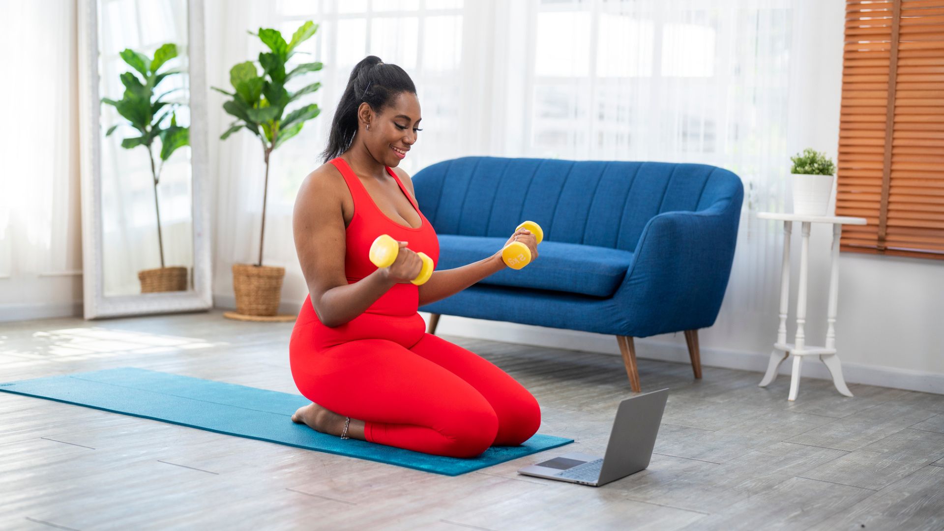 woman sits on knees on mat doing bicep curls with dumbbells