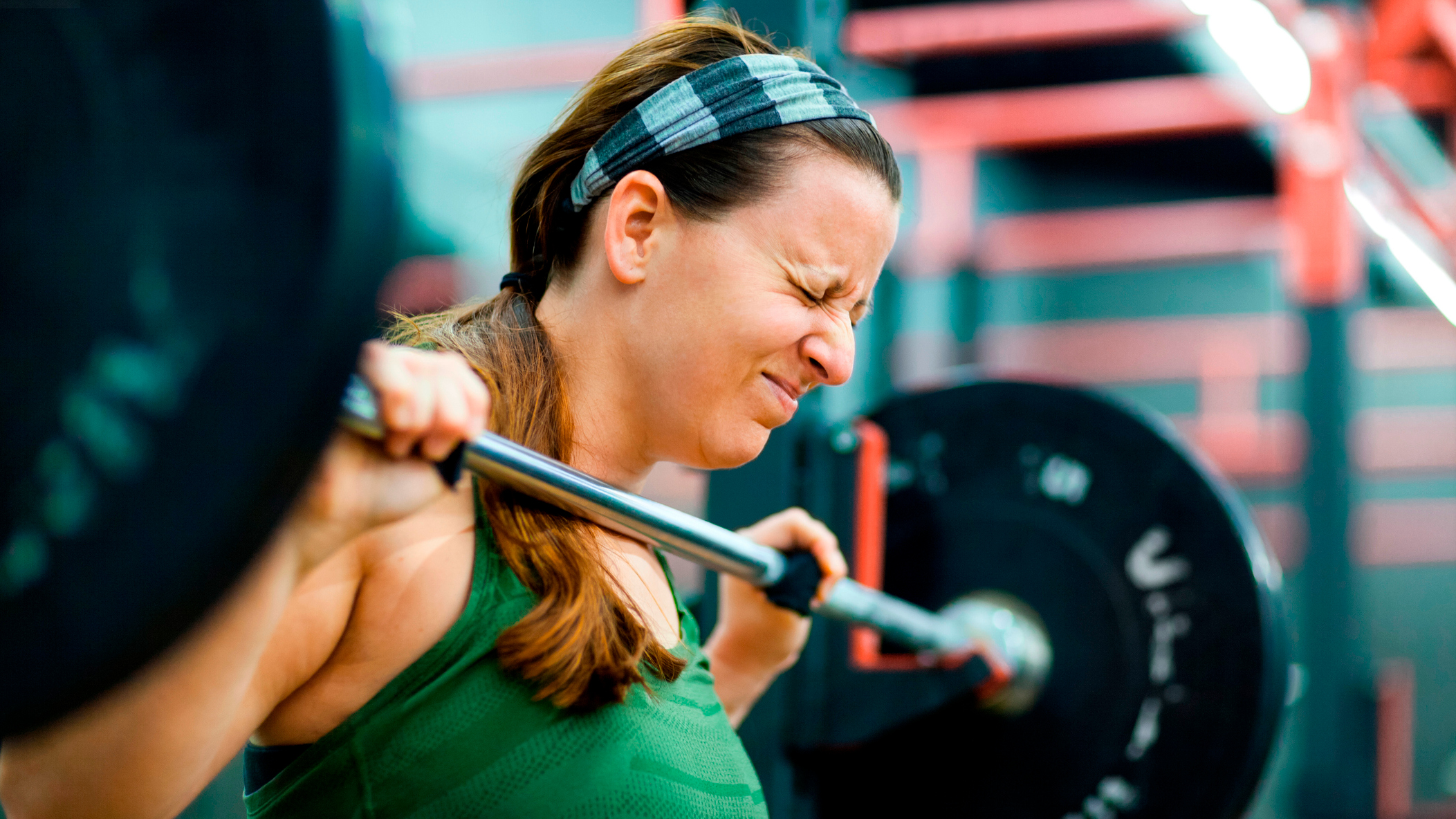 Woman holding barbell with face screwed up with effort